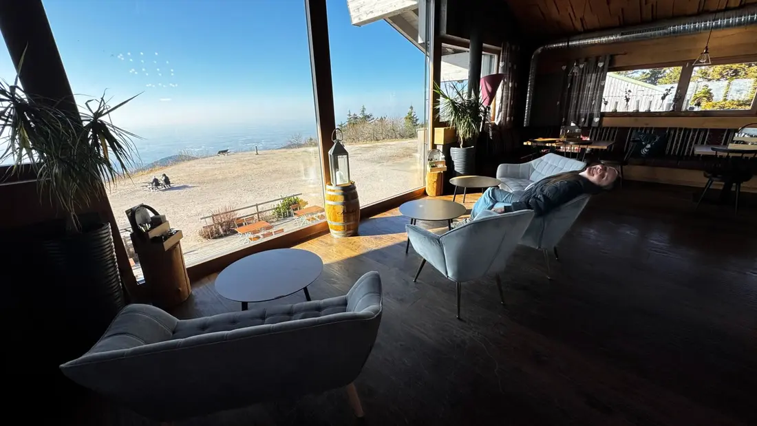 Gemütliche Lounge im Inneren der Grindehütte mit Sofas, Panoramafenstern und Blick über das Gipfelplateau der Hornisgrinde.